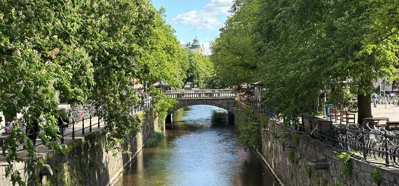 Fyrisån i centrala Uppsala en sommardag med grönskande träd längs kajerna och en stenbro
